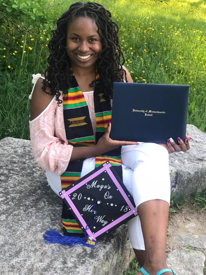 Photo of the global correspondent, Maya, sitting down holding her graduation cap