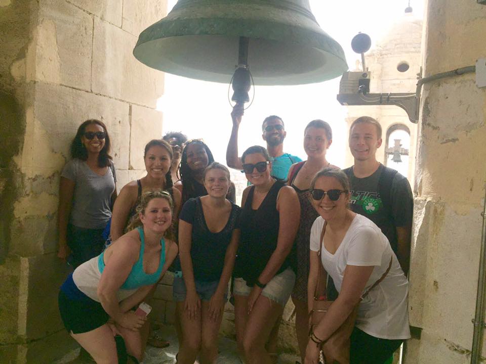 students pose for photo under the bell at the top of Vejer Cathedral in Cadiz, Spain