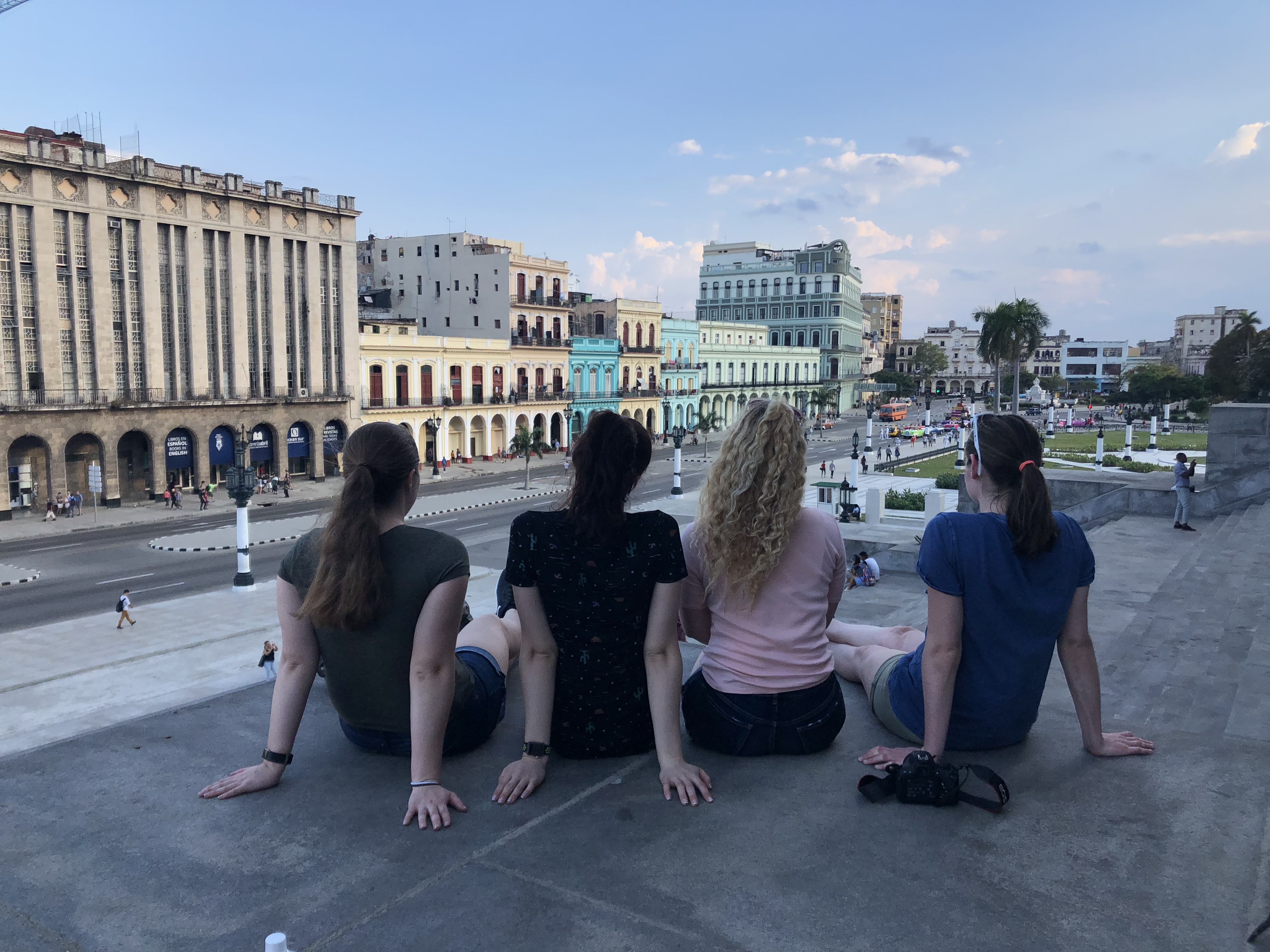 Honors students sit with their back to the camera on the steps of Cuba's capital building as they look out at the city.